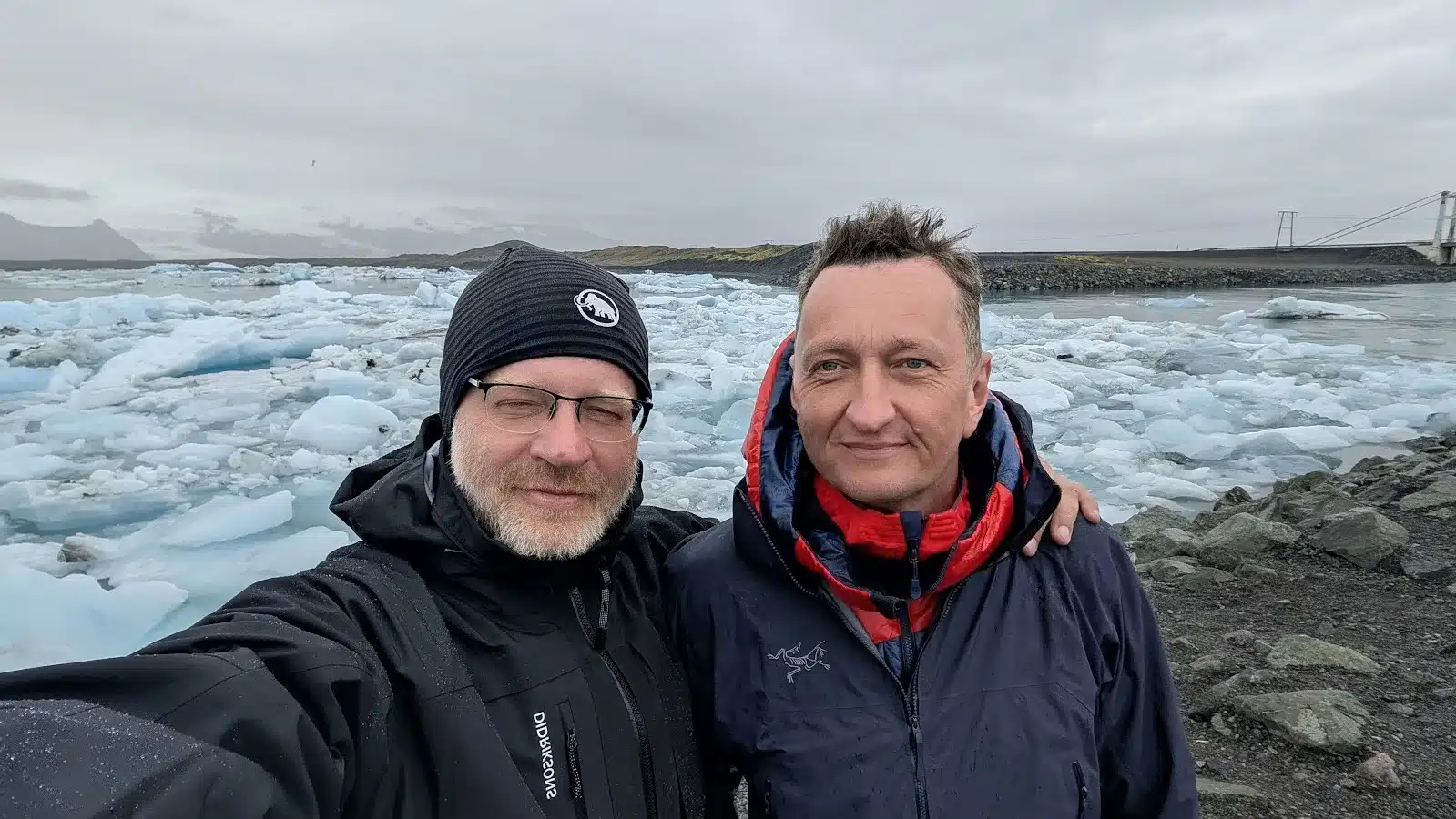 Two friends smiling at a glacier lagoon with floating icebergs, Iceland