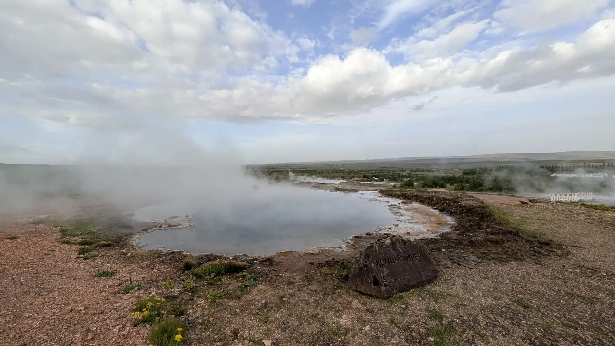 Steam rising from a geothermal pool under a cloudy Icelandic sky