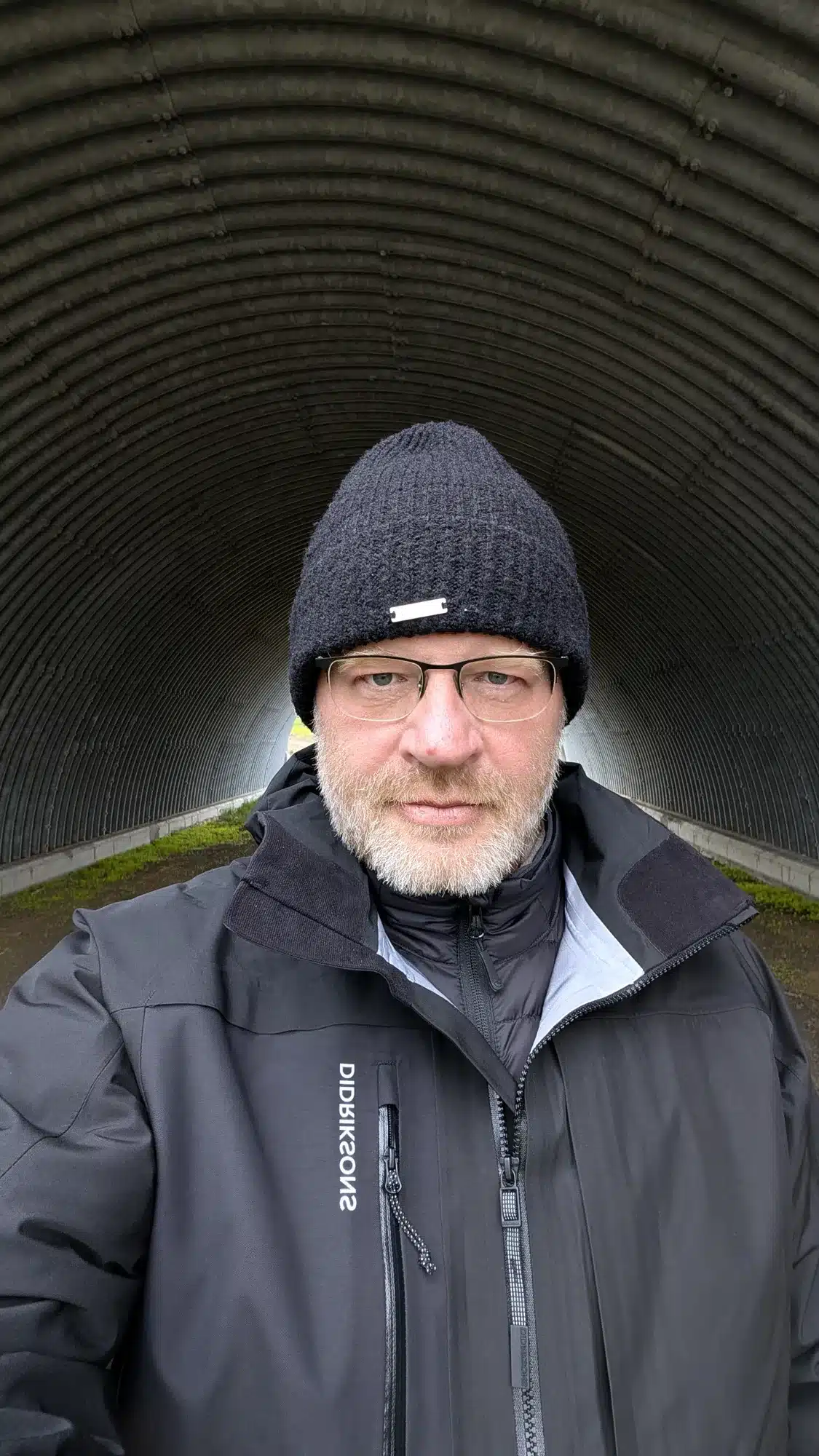 Bearded man in a black beanie inside a corrugated metal tunnel, Iceland